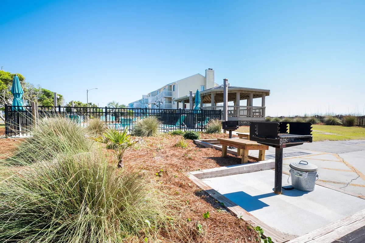 This image captures the outdoor recreation area, featuring a grill, picnic table, swimming pool, and surrounding greenery. The building is visible in the background, creating a clear sense of place and community.