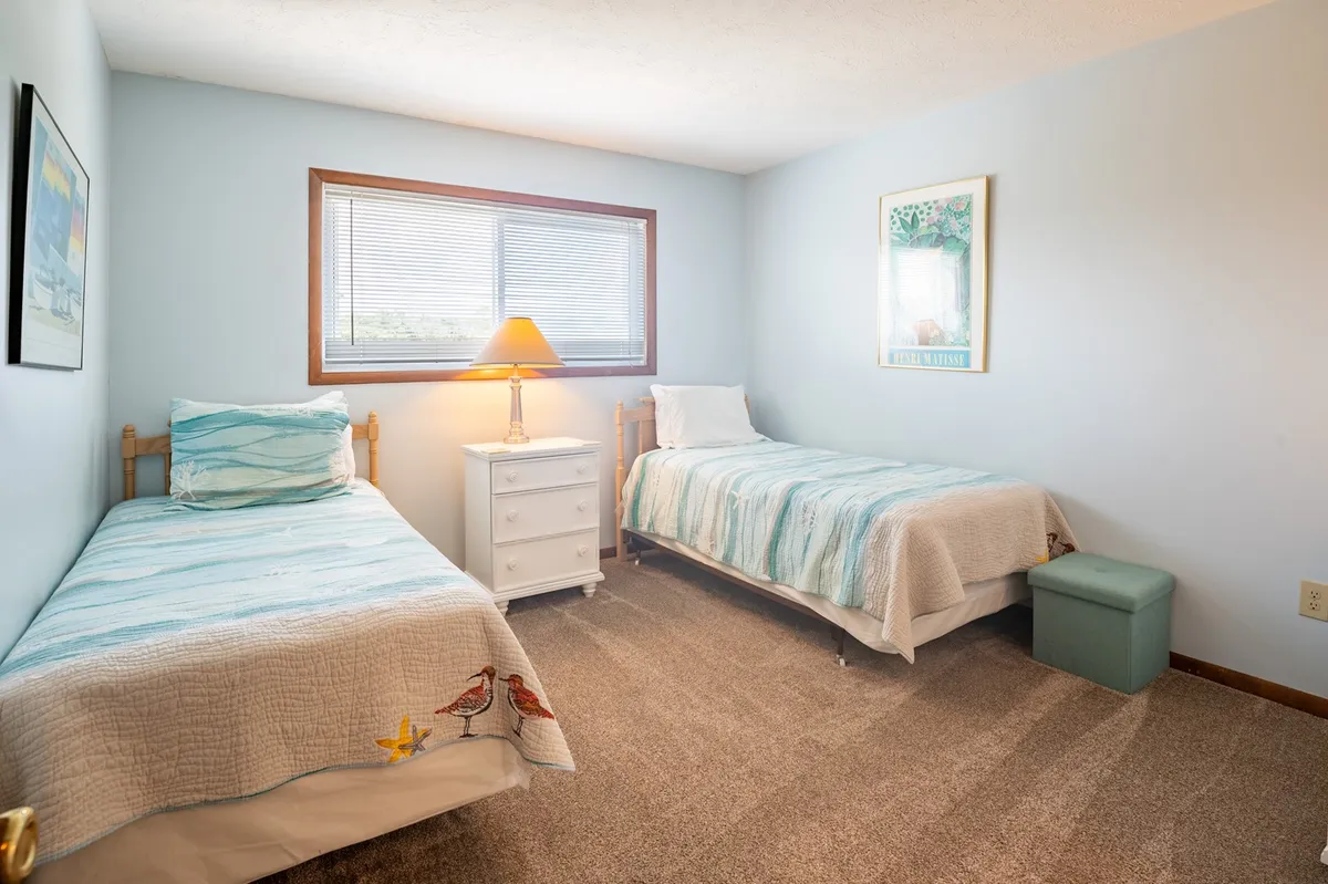 A cozy guest bedroom with two twin beds, a nightstand with a lamp, and decorative wall art. The room exudes a tranquil and inviting mood, perfect for guests or children seeking a restful night's sleep.
