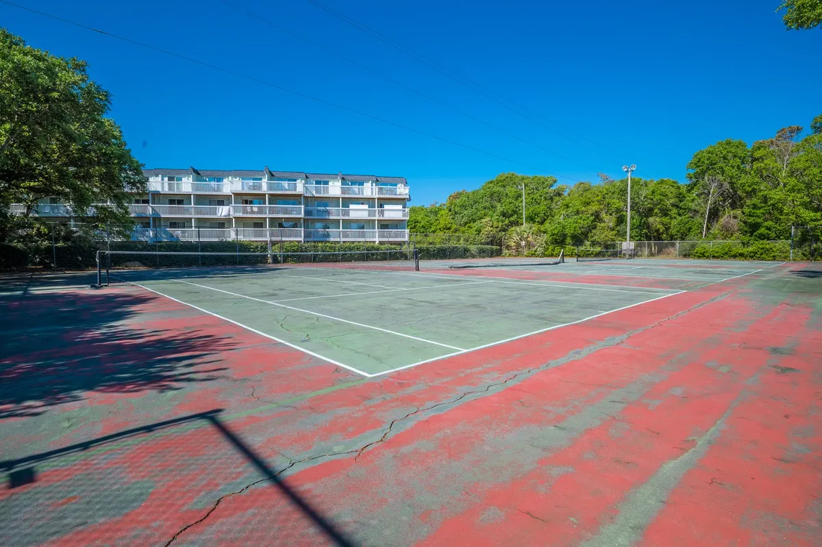 An exterior view of tennis courts surrounded by lush greenery and adjacent apartment buildings. The scene feels vibrant and inviting, encouraging recreation and community engagement.