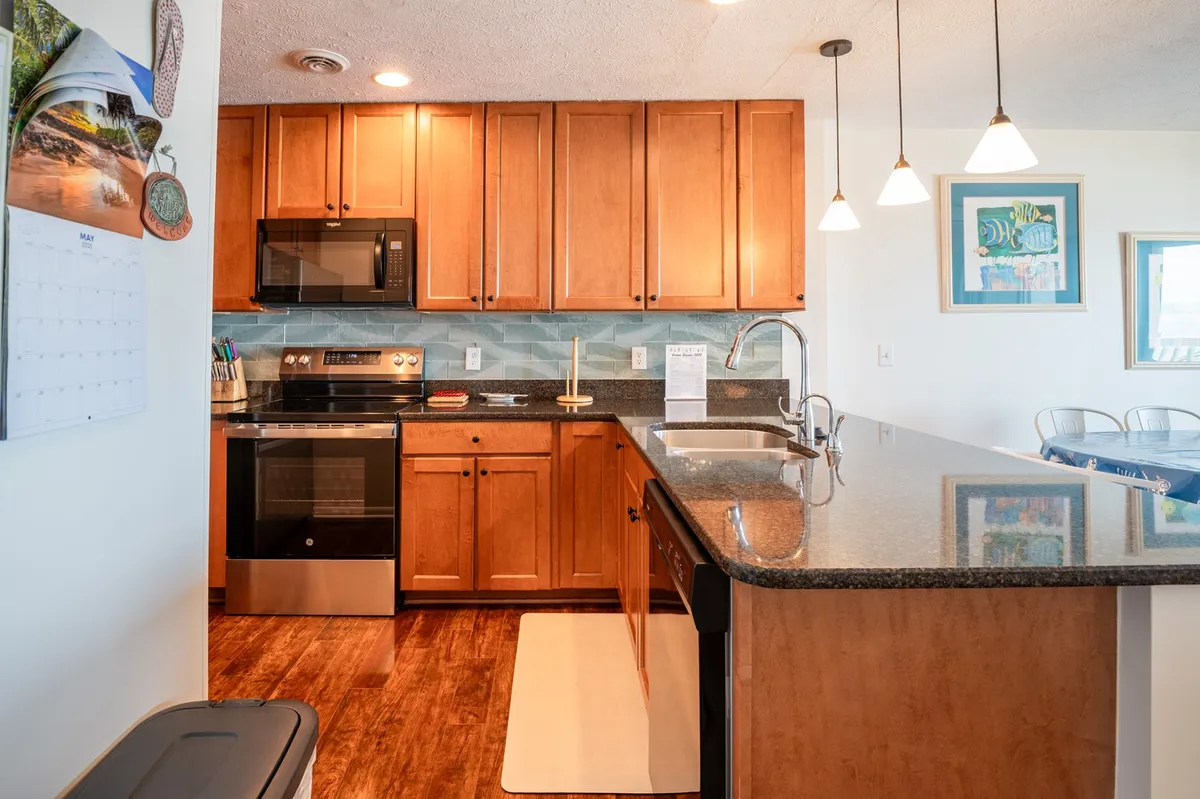 A warm, welcoming kitchen interior with granite countertops, wood cabinetry, modern appliances, and stylish pendant lighting over the workspaces. The setting is ideal for family gatherings, recipe sharing, and preparing both quick snacks and elaborate meals.