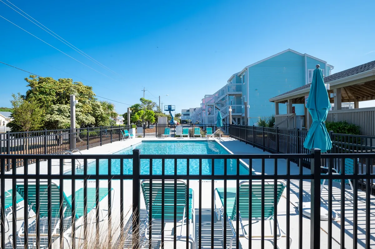 A sunny outdoor swimming pool with lounge chairs and umbrellas, surrounded by a fence, offering a relaxing and enjoyable place for swimming, sunbathing, and unwinding with friends or family.