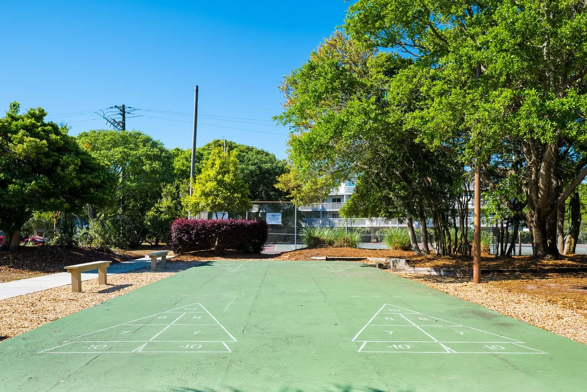 Outdoor shuffleboard courts set among lush greenery with benches nearby for relaxing. The courts invite playful competition and social interaction in a casual, friendly setting.