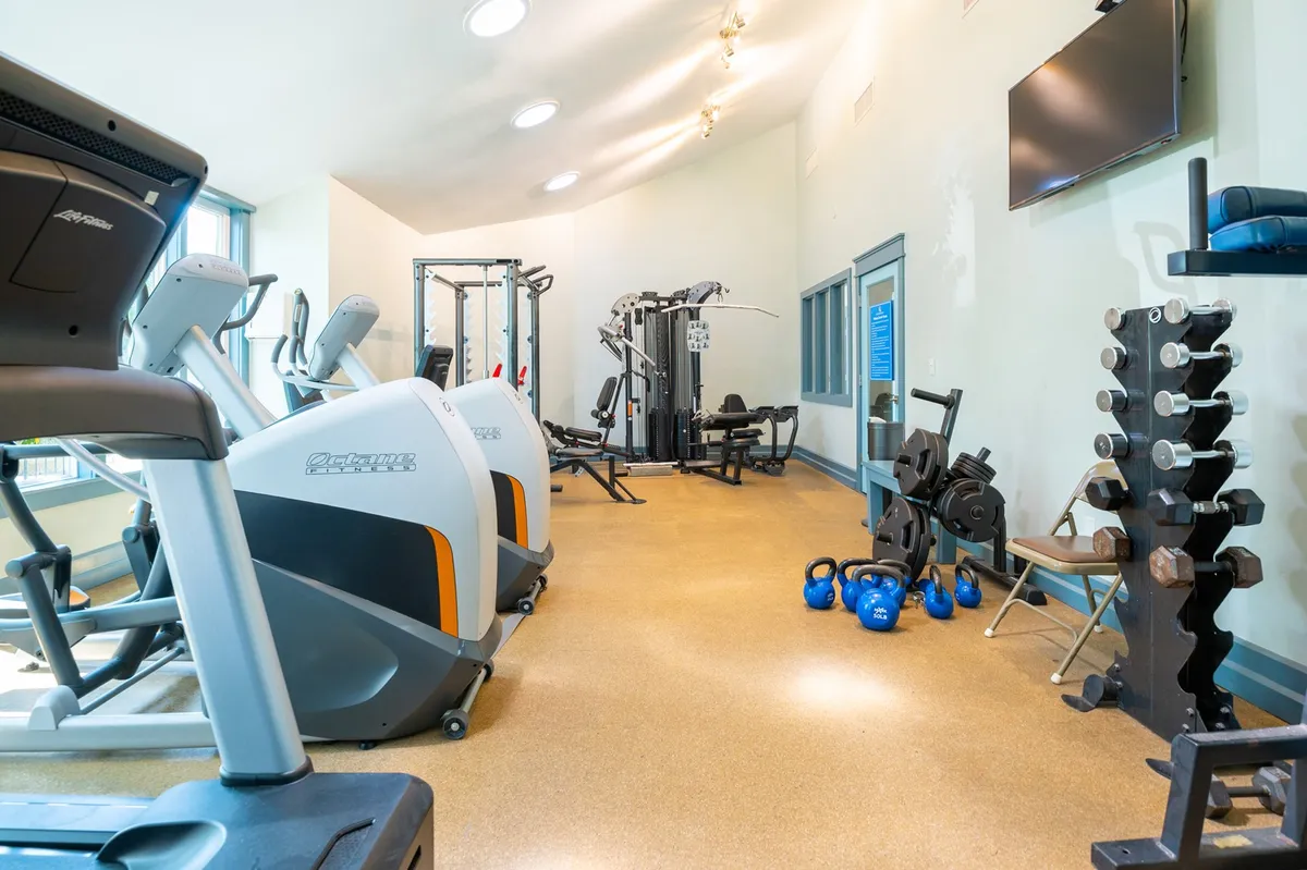 A modern fitness center featuring treadmills, weight machines, free weights, and kettlebells. The room is bright and well-equipped, demonstrating the kind of facility guests can expect for their workouts.