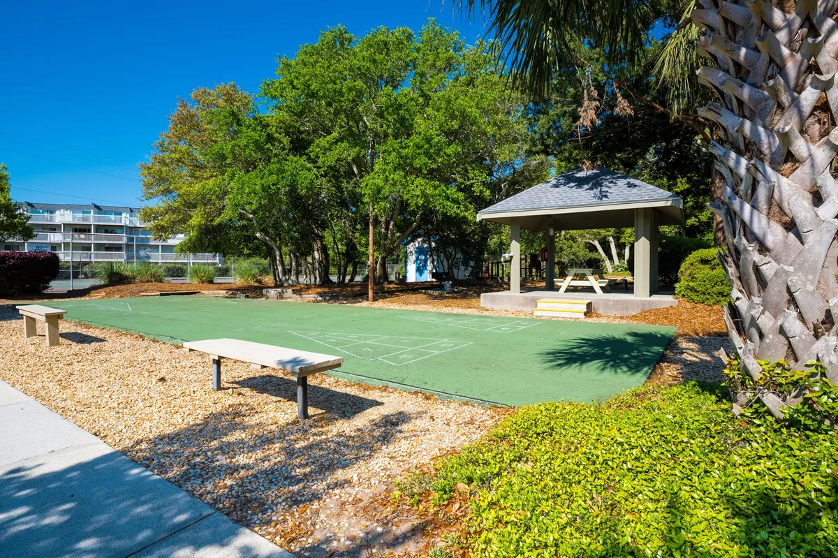 A vibrant outdoor recreation space with a green playing surface, gazebo, benches, and lush trees, inviting guests to enjoy group games, relax, or gather under the shade.